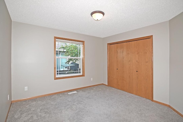 unfurnished bedroom with carpet, a textured ceiling, baseboards, and a closet