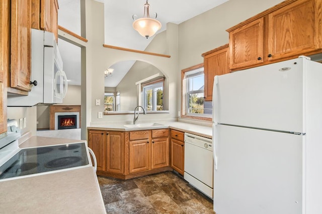 kitchen featuring light countertops, brown cabinetry, a sink, a warm lit fireplace, and white appliances