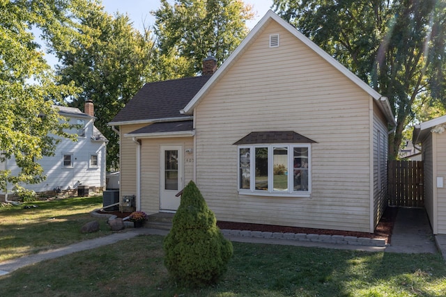 rear view of property featuring fence, roof with shingles, a chimney, central AC unit, and a yard