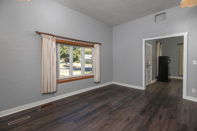 unfurnished room featuring vaulted ceiling, dark wood-style floors, and visible vents