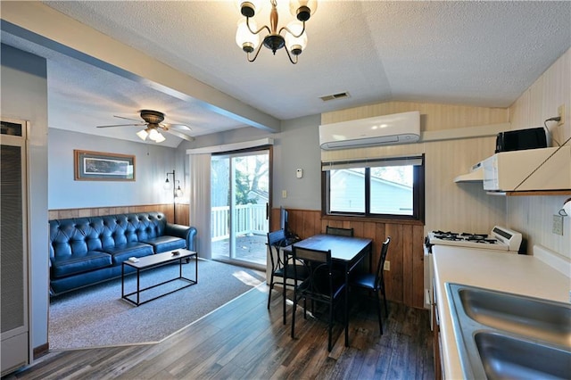 interior space with visible vents, dark wood-style floors, a textured ceiling, a wall unit AC, and vaulted ceiling