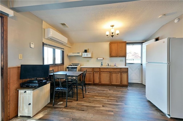 kitchen with an inviting chandelier, white appliances, a wall mounted air conditioner, brown cabinets, and a sink