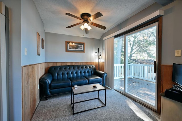 carpeted living room with a textured ceiling, wood walls, ceiling fan, and a wainscoted wall