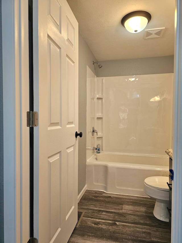 bathroom featuring tub / shower combination, hardwood / wood-style floors, a textured ceiling, and toilet