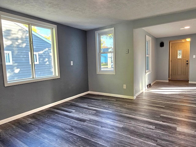 unfurnished room featuring a wealth of natural light, a textured ceiling, and dark hardwood / wood-style floors