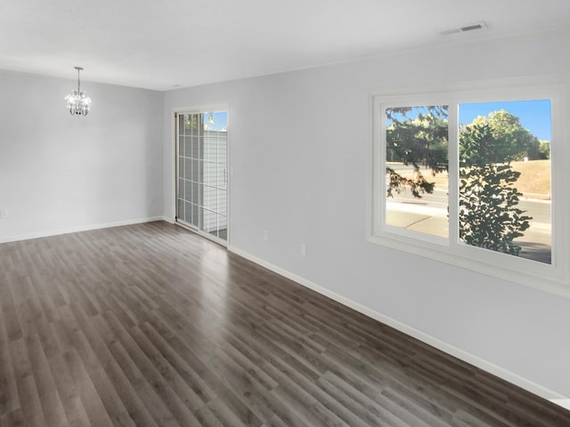 spare room featuring a notable chandelier, dark wood-type flooring, and a wealth of natural light