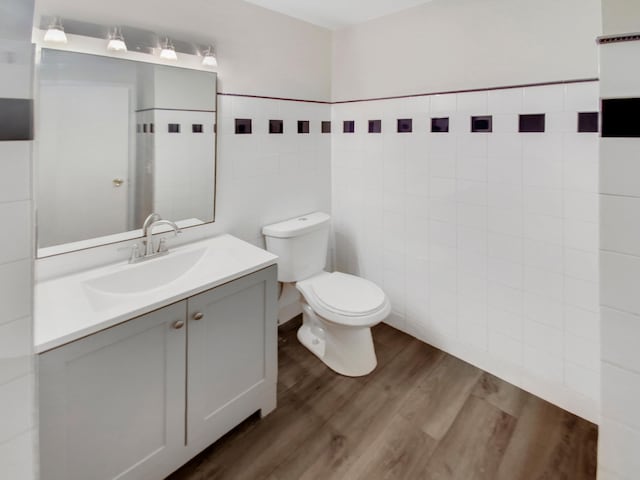 bathroom featuring wood-type flooring, vanity, tile walls, and toilet