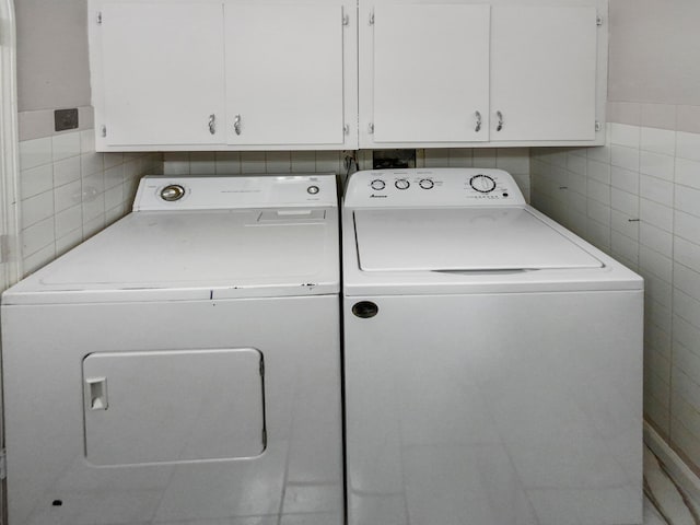 clothes washing area with washer and clothes dryer, cabinets, and tile walls