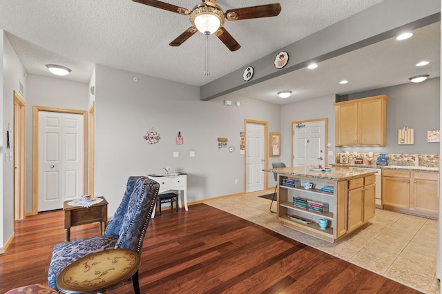 kitchen with light hardwood / wood-style floors, a textured ceiling, a kitchen island, ceiling fan, and light brown cabinetry