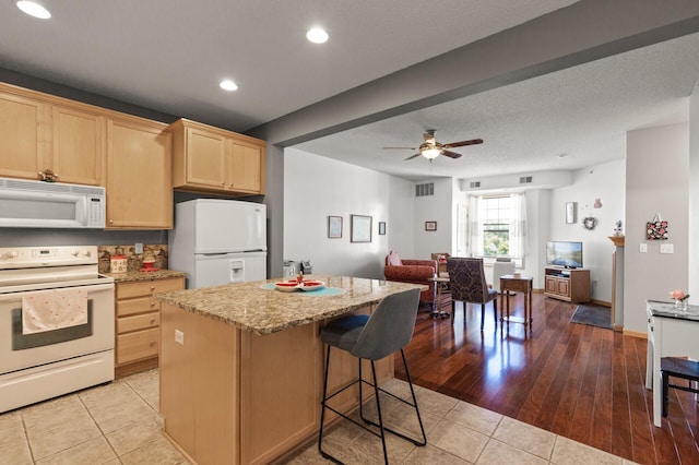 kitchen featuring ceiling fan, white appliances, a kitchen island, light hardwood / wood-style flooring, and light brown cabinetry