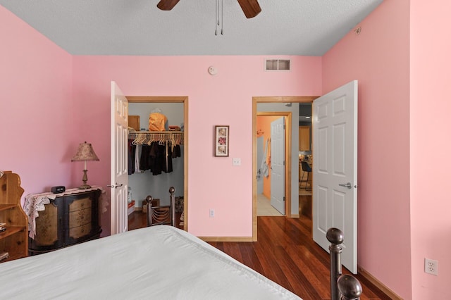 bedroom with a closet, a textured ceiling, ceiling fan, a walk in closet, and dark hardwood / wood-style floors