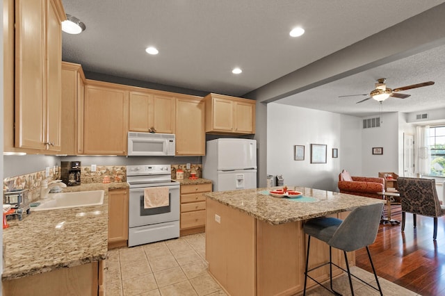 kitchen with light hardwood / wood-style floors, white appliances, a kitchen island, ceiling fan, and sink