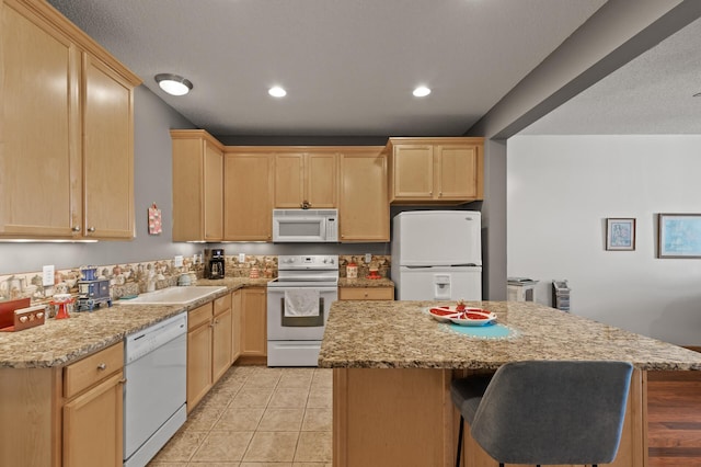 kitchen featuring sink, a kitchen island, white appliances, light brown cabinets, and light stone countertops