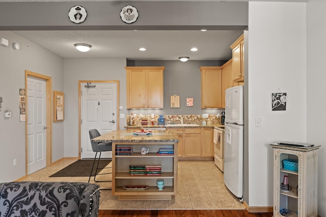 kitchen with light stone counters, sink, a breakfast bar area, white appliances, and light brown cabinetry