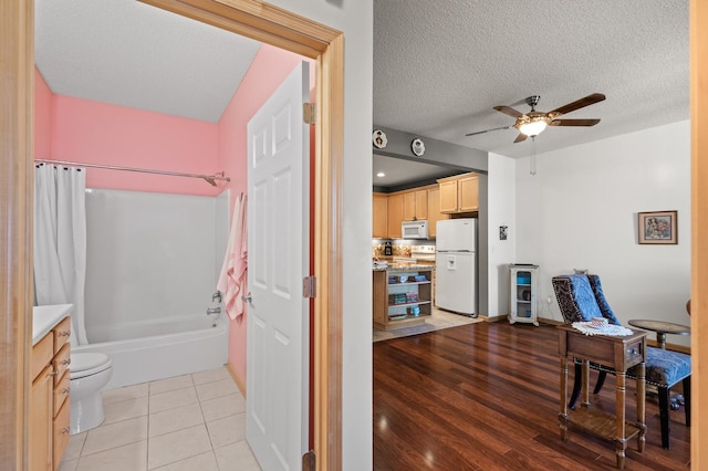 full bathroom featuring ceiling fan, toilet, a textured ceiling, hardwood / wood-style floors, and shower / tub combo with curtain