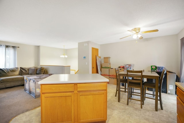 kitchen with light carpet, pendant lighting, ceiling fan with notable chandelier, and a center island