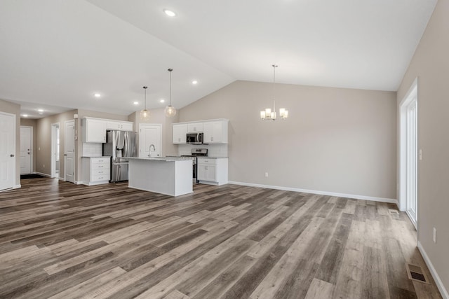 kitchen featuring tasteful backsplash, a kitchen island with sink, stainless steel appliances, and decorative light fixtures