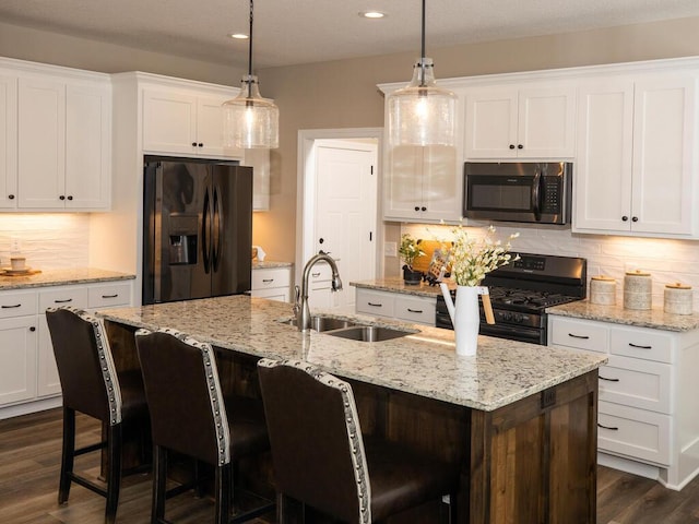 kitchen with dark wood-style flooring, stainless steel appliances, a sink, an island with sink, and white cabinets