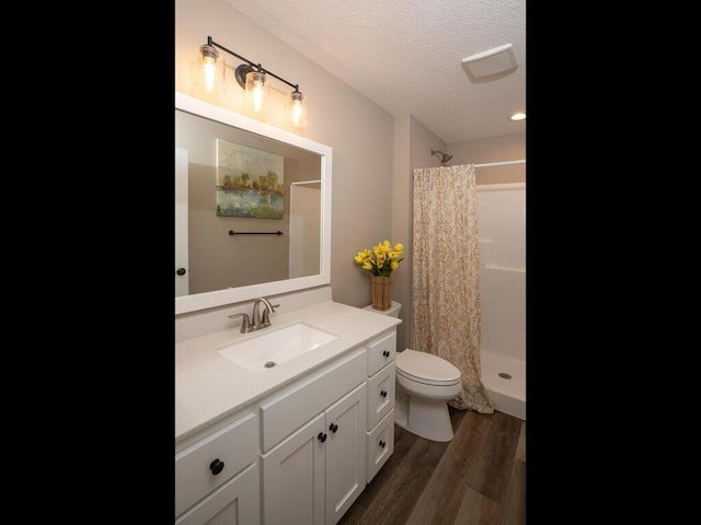 bathroom featuring a textured ceiling, a shower stall, toilet, wood finished floors, and vanity
