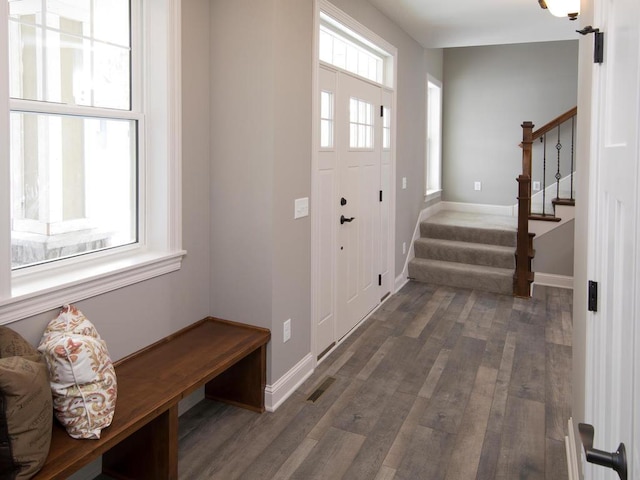 foyer featuring baseboards, visible vents, wood finished floors, and stairway