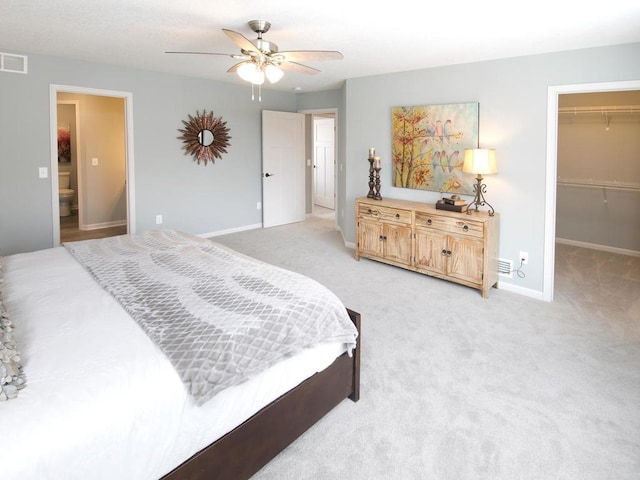 bedroom featuring visible vents, baseboards, a ceiling fan, a walk in closet, and light colored carpet