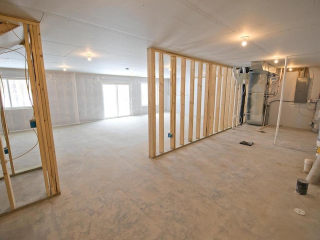 basement with electric panel, heating unit, and a healthy amount of sunlight