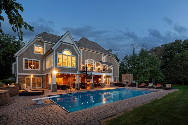 back house at dusk featuring a lawn, a balcony, and a patio area