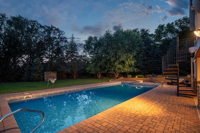 pool at dusk with a diving board, a yard, and a patio