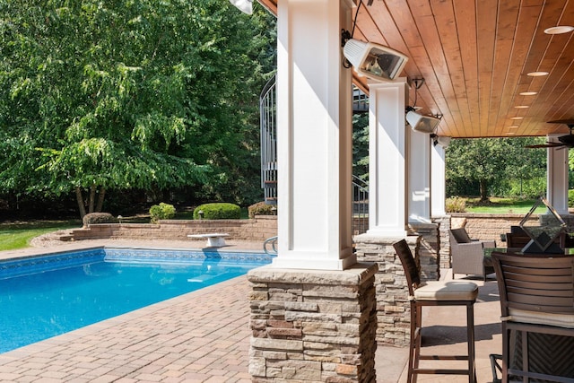 view of swimming pool with ceiling fan, a diving board, and a patio