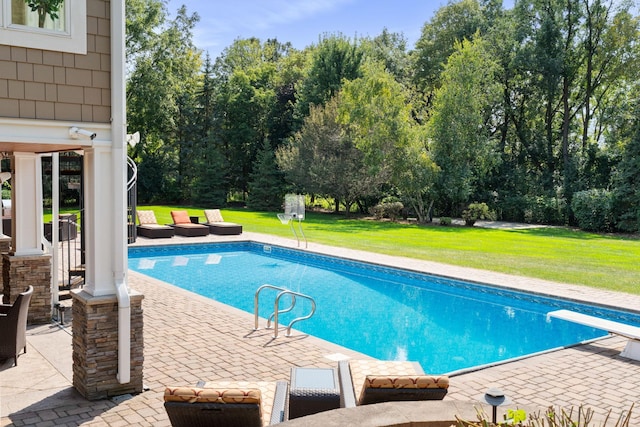 view of pool with a diving board, a lawn, and a patio area