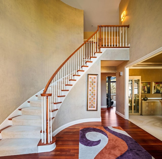 staircase featuring ornamental molding, a high ceiling, and hardwood / wood-style floors