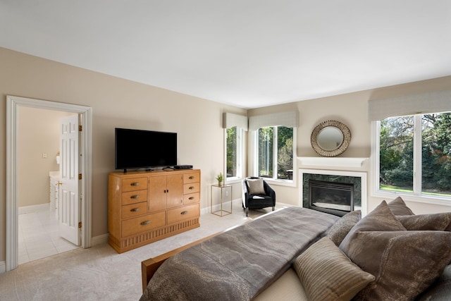 bedroom with light carpet, ensuite bathroom, a high end fireplace, and multiple windows