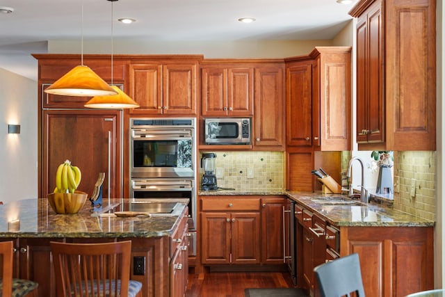 kitchen with appliances with stainless steel finishes, dark stone counters, decorative light fixtures, and sink