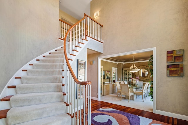 staircase featuring ornamental molding, a high ceiling, and wood-type flooring