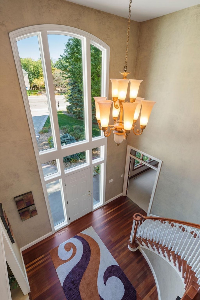 foyer entrance featuring a towering ceiling, dark hardwood / wood-style floors, a notable chandelier, and a healthy amount of sunlight