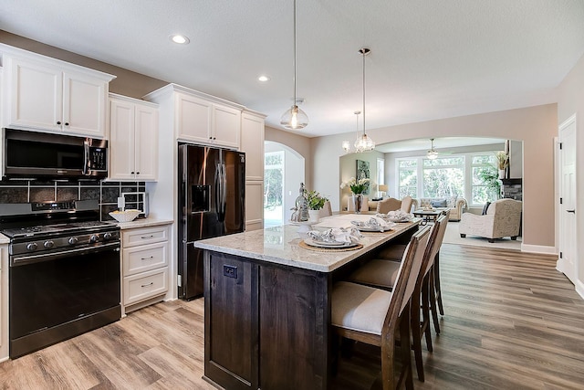 kitchen with ceiling fan, black gas stove, fridge with ice dispenser, white cabinetry, and a center island