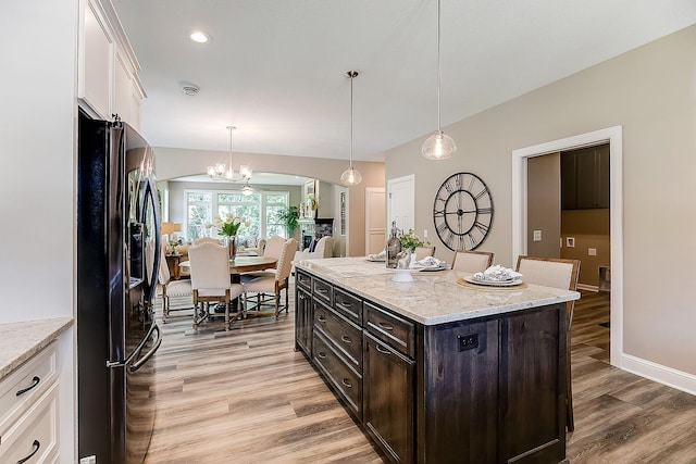 kitchen with light wood-type flooring, black fridge, white cabinets, a kitchen island, and decorative light fixtures