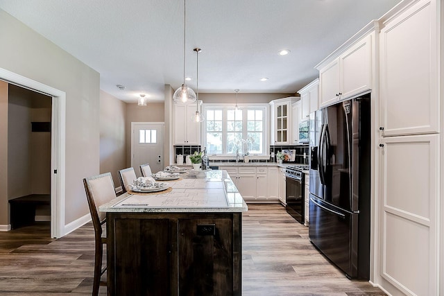 kitchen with white cabinetry, a breakfast bar, pendant lighting, black appliances, and a center island