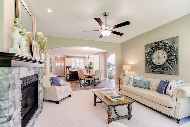 living room with a stone fireplace, hardwood / wood-style flooring, and ceiling fan with notable chandelier