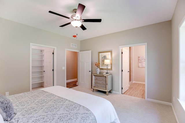 bedroom with ceiling fan, light colored carpet, a closet, and a walk in closet