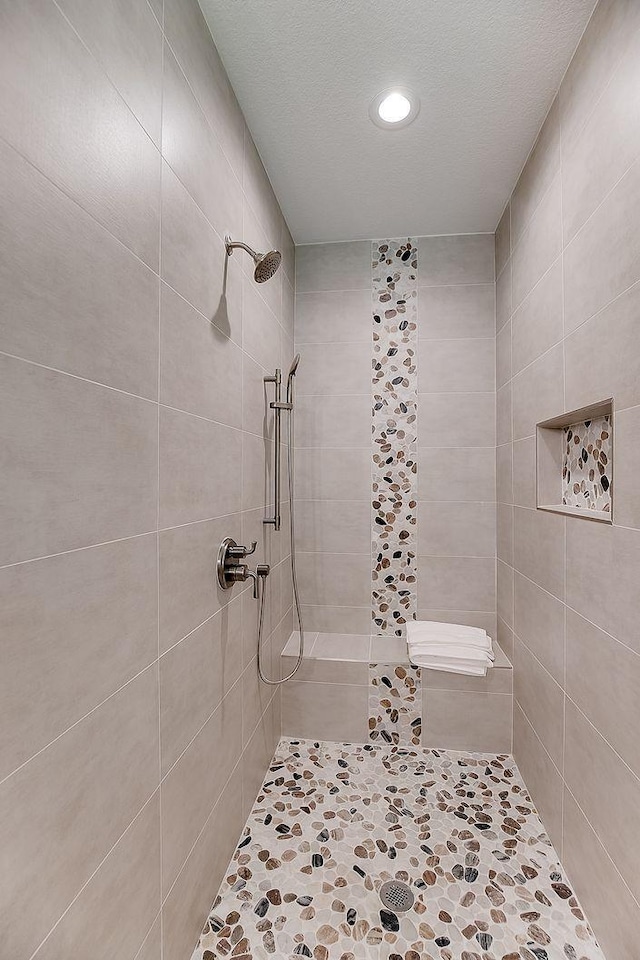 bathroom with a textured ceiling and a tile shower