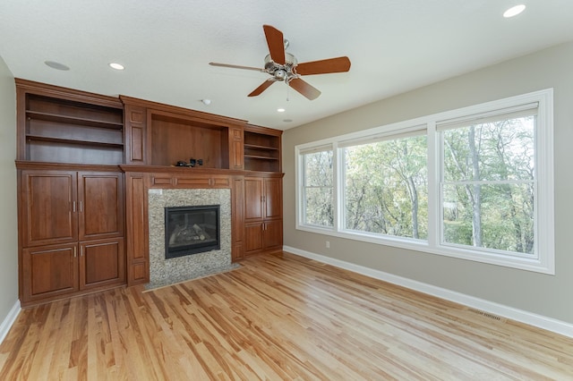 unfurnished living room featuring a premium fireplace, light hardwood / wood-style flooring, ceiling fan, and plenty of natural light