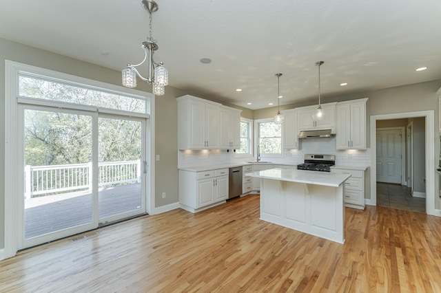 kitchen featuring white cabinets, appliances with stainless steel finishes, light hardwood / wood-style flooring, decorative light fixtures, and a center island