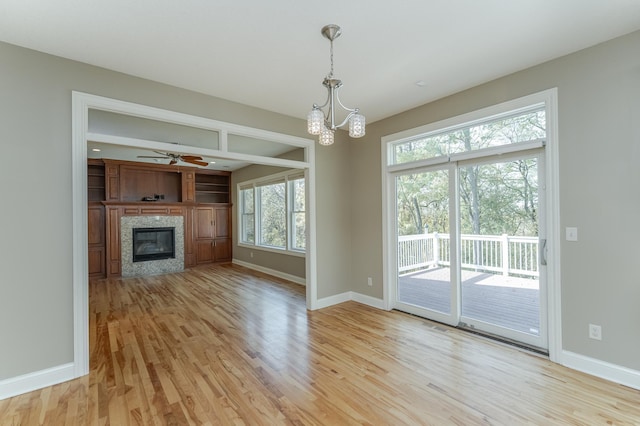 unfurnished living room with ceiling fan with notable chandelier, plenty of natural light, and light wood-type flooring