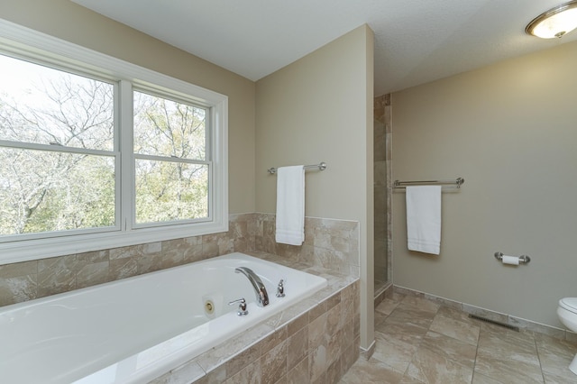 bathroom with a textured ceiling, a relaxing tiled tub, and toilet