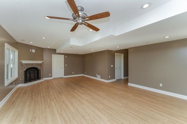 unfurnished living room with a tile fireplace, light wood-type flooring, and ceiling fan