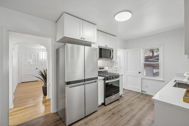 kitchen featuring appliances with stainless steel finishes, sink, white cabinets, light stone counters, and light hardwood / wood-style floors