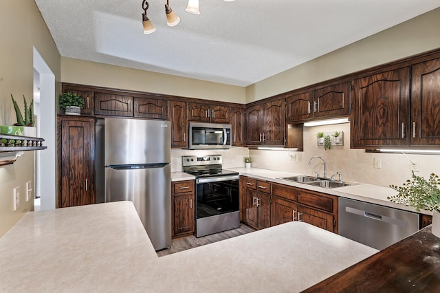 kitchen with dark brown cabinetry, appliances with stainless steel finishes, light countertops, a textured ceiling, and a sink