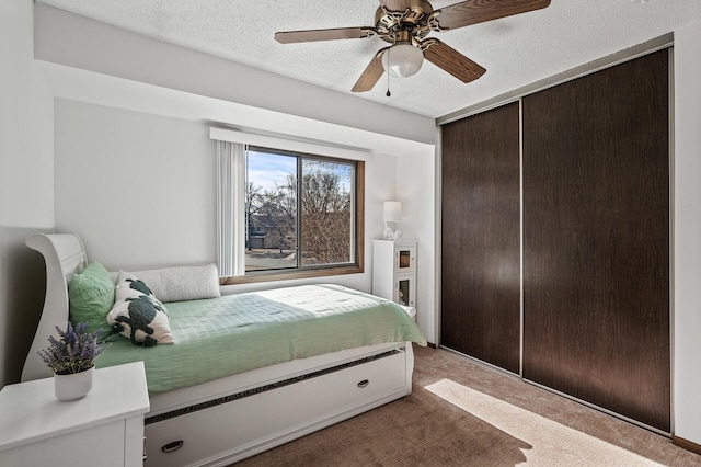 carpeted bedroom featuring a closet, a ceiling fan, and a textured ceiling