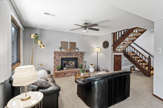 carpeted living area with visible vents, a ceiling fan, stairs, a textured ceiling, and a fireplace